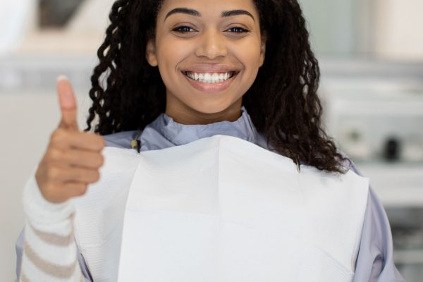 young dark-haired woman in dental chair gives thumbs up to camera